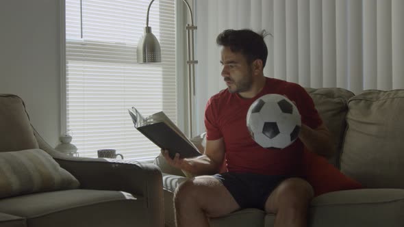 Man Holding Soccer Ball While Learning Soccer Moves From a Book