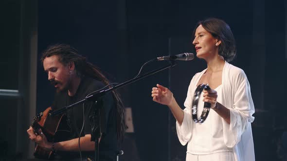 Female Singer with Tambourine and Musician Playing Guitar Performing on Stage