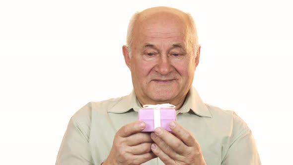 Happy Old Man Smiling Joyfully Holding Out a Gift Box To the Camera