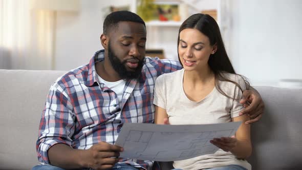 Young Multiracial Family Looking at Building Plan, Choosing Interior Design