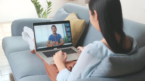 Woman Greeting With Colleagues In Video Conference From Laptop At Home Living Room