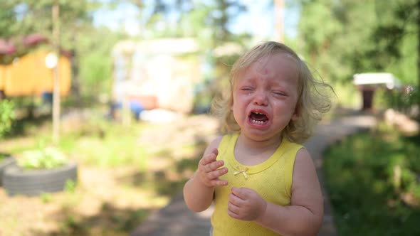 Close Up Portrait of Little Funny Cute Blonde Girl Child Toddler in Yellow Bodysuit Crying Outside