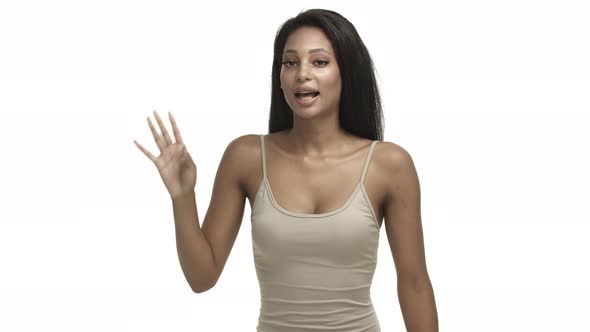 Coquettish Africanamerican Woman in Beige Tanktop Waving Hand and Saying Hello Greeting you with