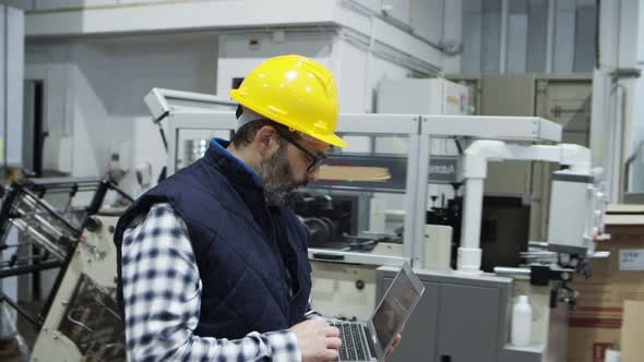 Side View of Serious Technician Walking with Laptop at Factory