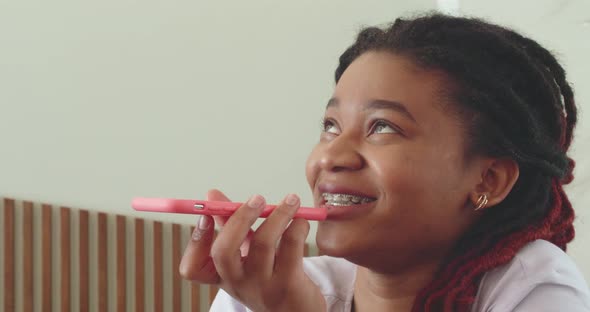 An AfricanAmerican Woman with Braces on Her Teeth Speaks on a Pink Smartphone She Holds Near Her