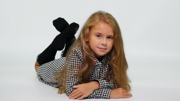 A Girl in a Checkered Dress Lies on the Floor, Gently Smiling at the Camera