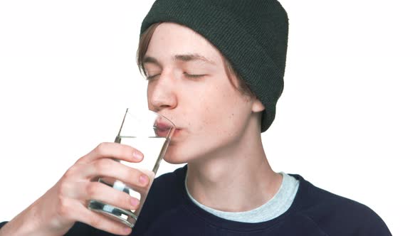 Portrait of Blueeyed Male Teenager with Clean Skin in Sweatshirt and Hat Drinking Still Water From