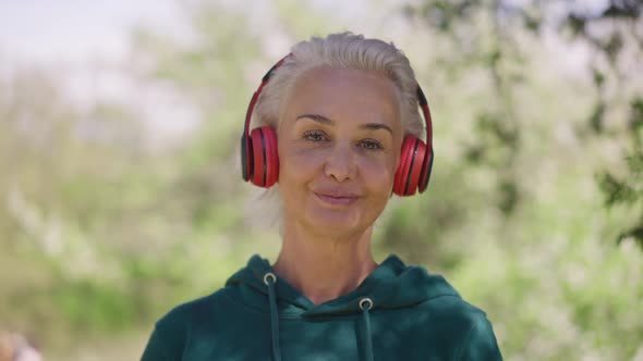 Closeup Portrait of Confident Senior Fit Sportswoman Putting on Headphones Looking at Camera and
