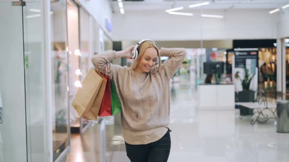 Pretty Blonde Is Having Fun in Shopping Mall Listening To Music Through Headphones