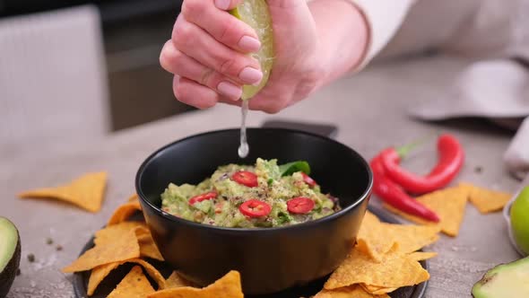 Woman Squeezing Fresh Lime Juice Into Freshly Made Guacamole on the Table