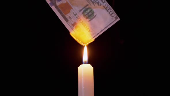 Burning 100 Dollar Bill Over a Smoky Candle Flame on a Black Background