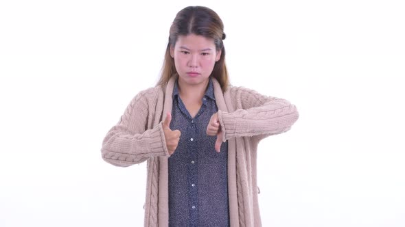 Confused Young Asian Woman Choosing Between Thumbs Up and Thumbs Down for Winter