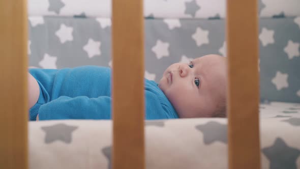 Funny Newborn Baby in Bodysuit Rests in Cozy Crib at Home