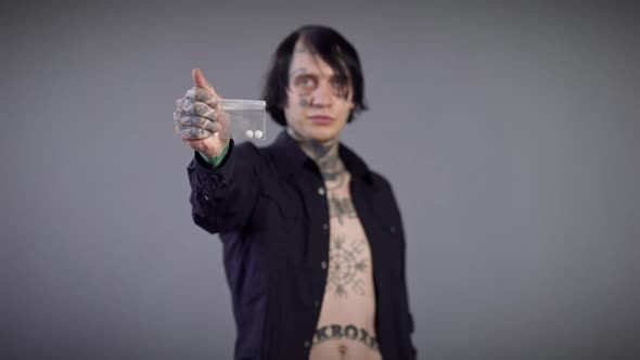 Closeup White Pills Drugs in Pack with Blurred Smiling Tattooed Young Man at Grey Background