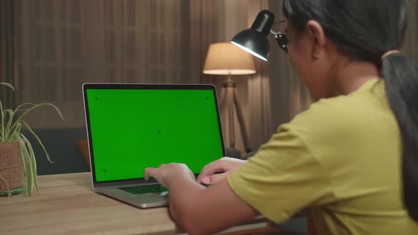 Asian Kid Girl Sitting In A Wheelchair While Using Laptop Computer With Mock Up Green Screen At Home