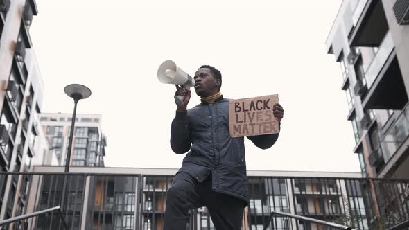 A Young Black Man Shouts Angrily with Megaphone and Holds a Sign Black Lives Matter