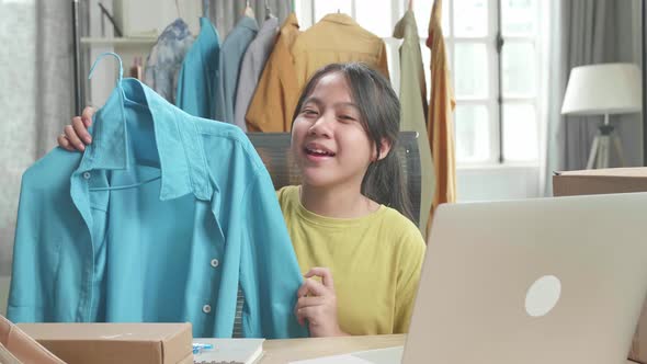 Asian Young Girl Online Seller Recommending A Shirt While Using Computer For Selling Clothes At Home