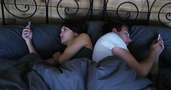 Couple ignoring each other and using mobile phone on bed