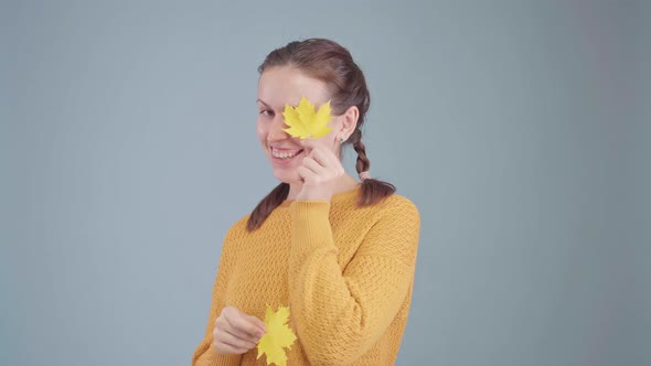 A happy girl in a yellow sweater closes her eyes with small yellow maple leaves