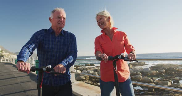 Senior couple walking next to electronic scooter alongside beach