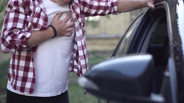 Unrecognizable Adult Caucasian Man Having Heart Attack Standing at Car Outdoors