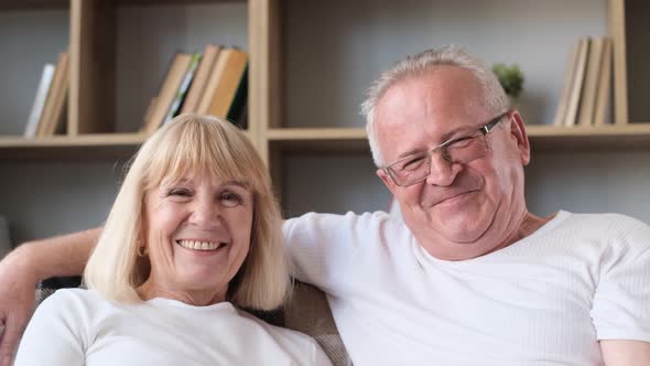 A Happy Elderly Couple is Sitting on the Sofa and Watching a Movie