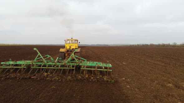 Aerial View of a Yellow Tractor with a Trailer Plowing a Land Plowing a Cultivated Field Before