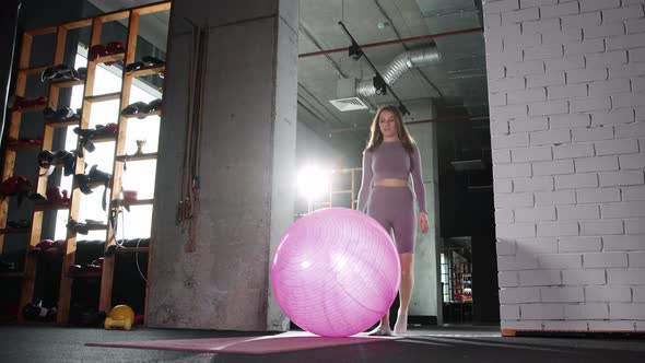 Young Woman Doing Pilates  Walks to the Fitness Ball  Sits Down on It and Starts an Exercise
