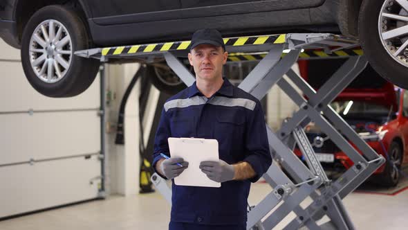 Man in Uniform in a Auto Repair Shop Standing with Tablet Ic Car Service