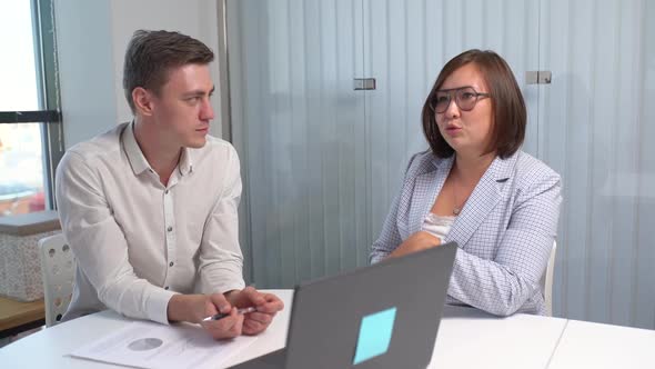 Two Colleagues Business Partners of Diverse Gender Race Sitting By Laptop at Office Workplace