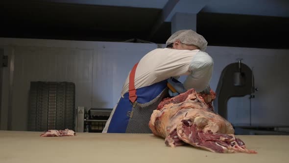 Butcher Cut Raw Meat with Knife at Table in Slaughterhouse