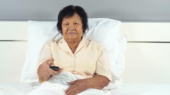 happy senior woman in bed with remote control and watching tv