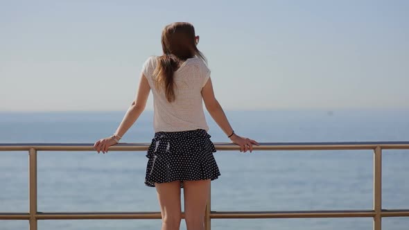 Rear View of a Thoughtful Beautiful Young Woman in Blue Skirt Contemplating the Sea on a Beach