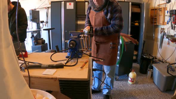 Two men working in a home garage metal shop - using an angle grinder to cut steel in slow motion