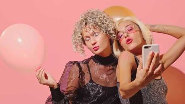 Young Beautiful Fashionable Women Make Selfies Together at Party Over Pink Wall.