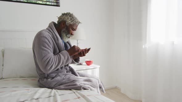 Senior man using smartphone while sitting on bed at home