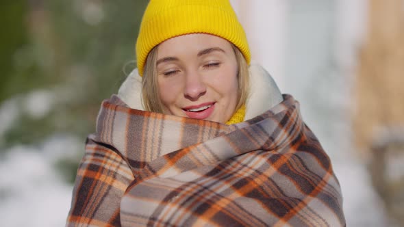 Headshot Portrait of Happy Young Woman in Yellow Hat Wrapping in Blanket Standing Outdoors Looking