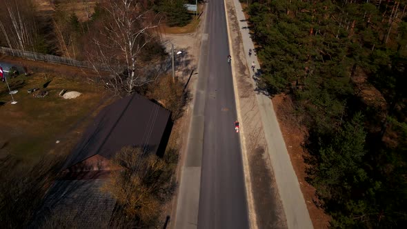 Aerial Follow Shot Behind Two Bicyclists Riding Along Country Road with Trees on Sides