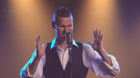 A Young Stylish Guy Vocalist Singing and Gestures with His Hands on Stage in a Vintage Microphone