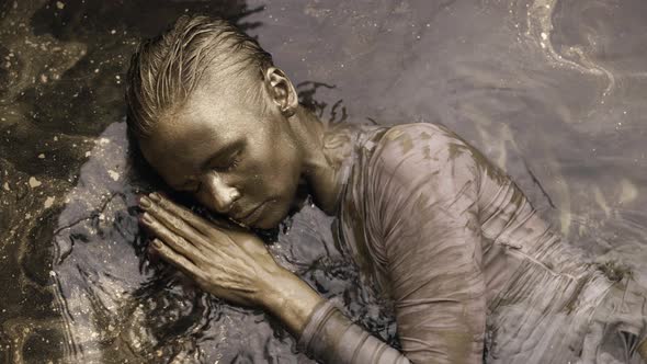 Artistic Shot with Golden Woman in Water with Shiny Pigment Gold Goddess Lady is Covered By Dye