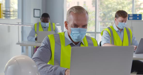 Diverse Engineers in Safety Mask Working on Laptop in Open Space Office