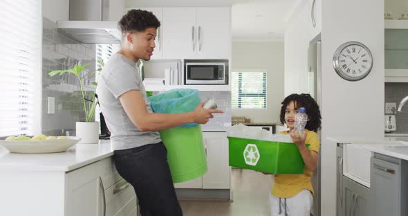 Happy biracial man and his son sorting waste in kitchen