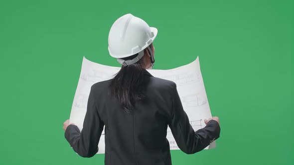 Back View Of Female Engineer Looking At Blueprint And Looking Around In The Green Screen Studio