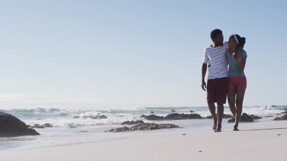 African american couple smiling, embracing and walking on the beach