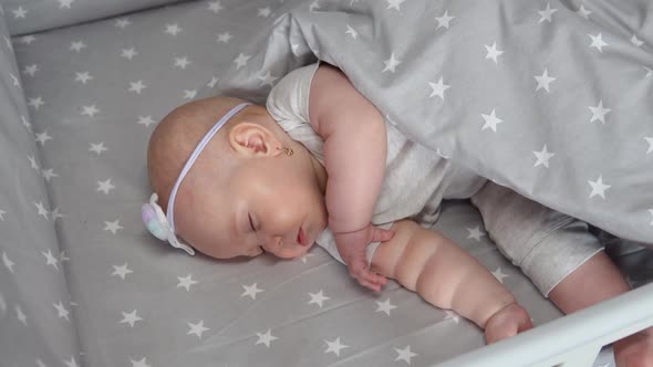 The Baby Girl Sleeps in a Crib with Rocking Gray Bed Linen