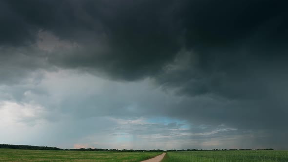 Dramatic Sky With Rain Clouds On Horizon Above Rural Landscape Country Road Through Field