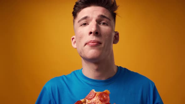 Close Up of a Guy Eating Pizza Slice Against Yellow Studio Background