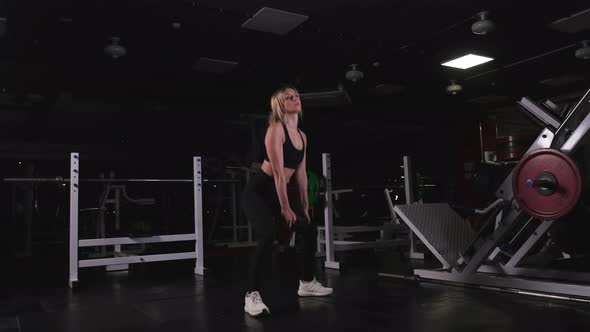 Slender Blonde Crouches with a Heavy Dumbbell