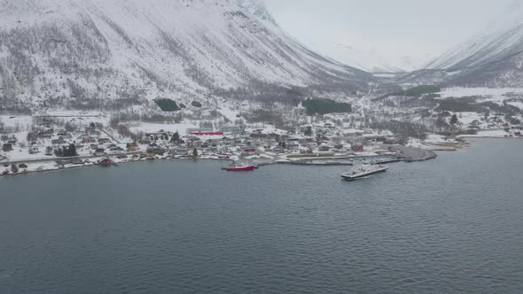 Boat departs snow covered Olderdalen ferry pier, arctic winter aerial view