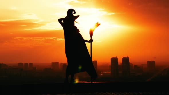 Silhouette Woman in Hat and Fluttering Cloak Holds Broom